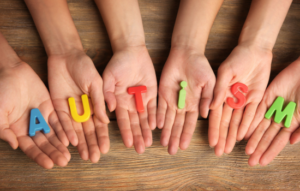 Five hands with letters spelling the word autism